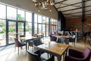 Bright and modern dining area at Grange Leisure Park near Mablethorpe, Lincolnshire, featuring floor-to-ceiling windows, exposed brick walls, and stylish furnishings, designed by Norfolk architects Paul Robinson Partnership