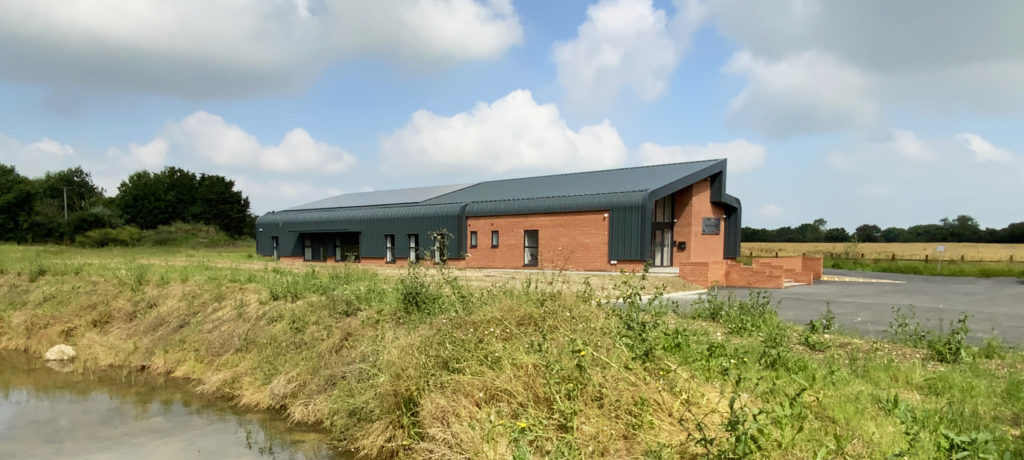 Contemporary new build office building in a rural Norfolk setting, designed by a Norwich-based architect. This project combines traditional red brickwork with modern steel cladding, creating a sleek and functional design that blends seamlessly with its natural surroundings. The building features a dynamic roofline and expansive glazing, providing a bright and welcoming workspace while maintaining a strong connection to the landscape.