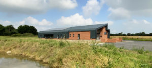 Contemporary new build office building in a rural Norfolk setting, designed by a Norwich-based architect. This project combines traditional red brickwork with modern steel cladding, creating a sleek and functional design that blends seamlessly with its natural surroundings. The building features a dynamic roofline and expansive glazing, providing a bright and welcoming workspace while maintaining a strong connection to the landscape.